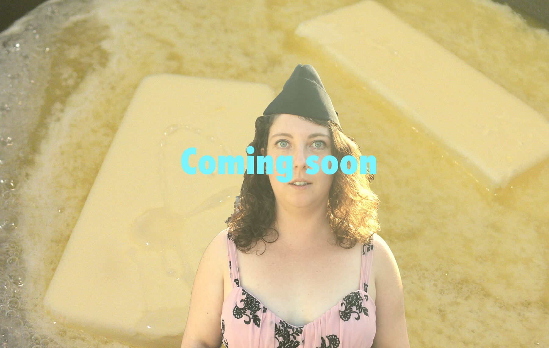 A person in a black garrison cap and a pink floral dress, standing in front of sticks of butter melting in a pan, with “Coming soon” written across the picture.